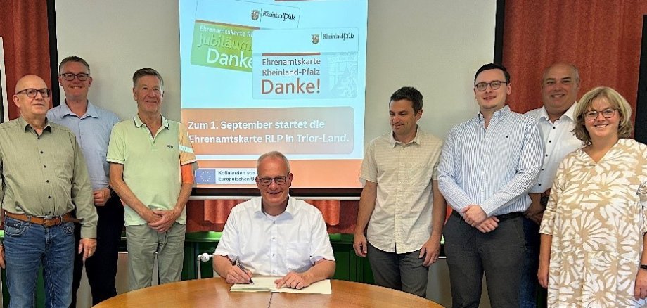 Bürgermeister Michael Holstein unterzeichnet den Kooperationsvertrag zwischen der Landesregierung Rheinland-Pfalz und der Verbandsgemeinde Trier-Land zur Einführung der landesweiten Ehrenamtskarte im Beisein Vertretern der Ortsgemeinden sowie Mitgliedern des Ältestenrates, die die Einführung der Ehrenamtskarte sehr begrüßen.