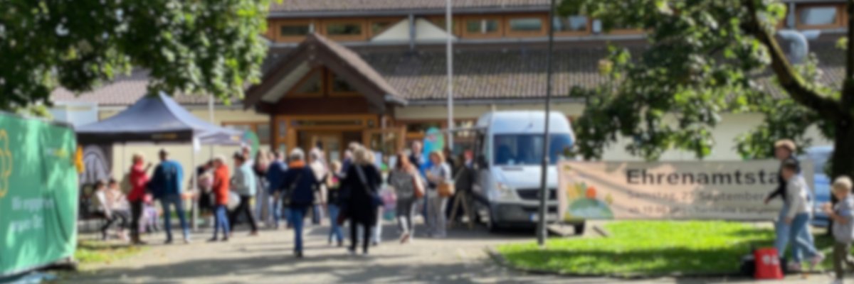 Unscharfes Bild von einer Veranstaltung. Rechts im Bild ist ein Banner mit dem Titel "Ehrenamtstag" erkennbar. 