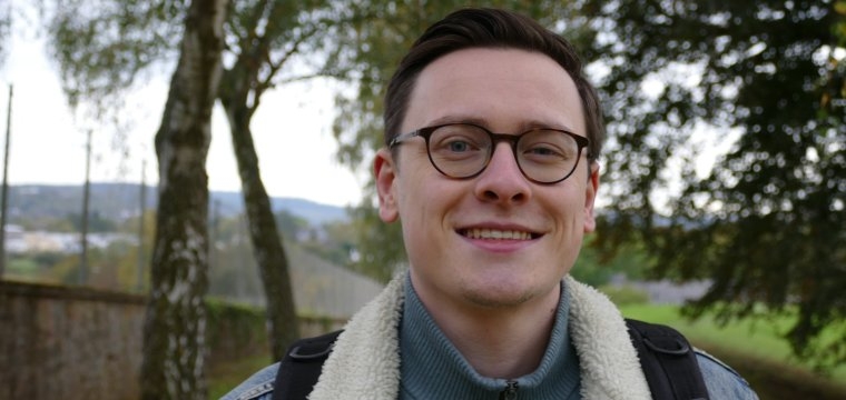 Person mit Jeansjacke. Im Hintergrund sind Bäume zu erkennen.