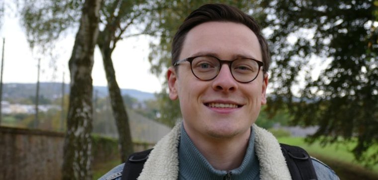 Person mit Jeansjacke. Im Hintergrund sind Bäume zu erkennen.